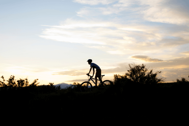 The silhouette of a mountain biker trekking along a rocky Colorado trail.